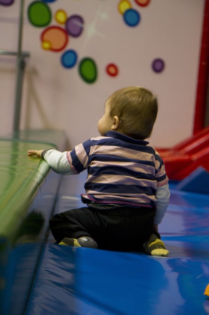 A young child sits on the floor holding on to a mat